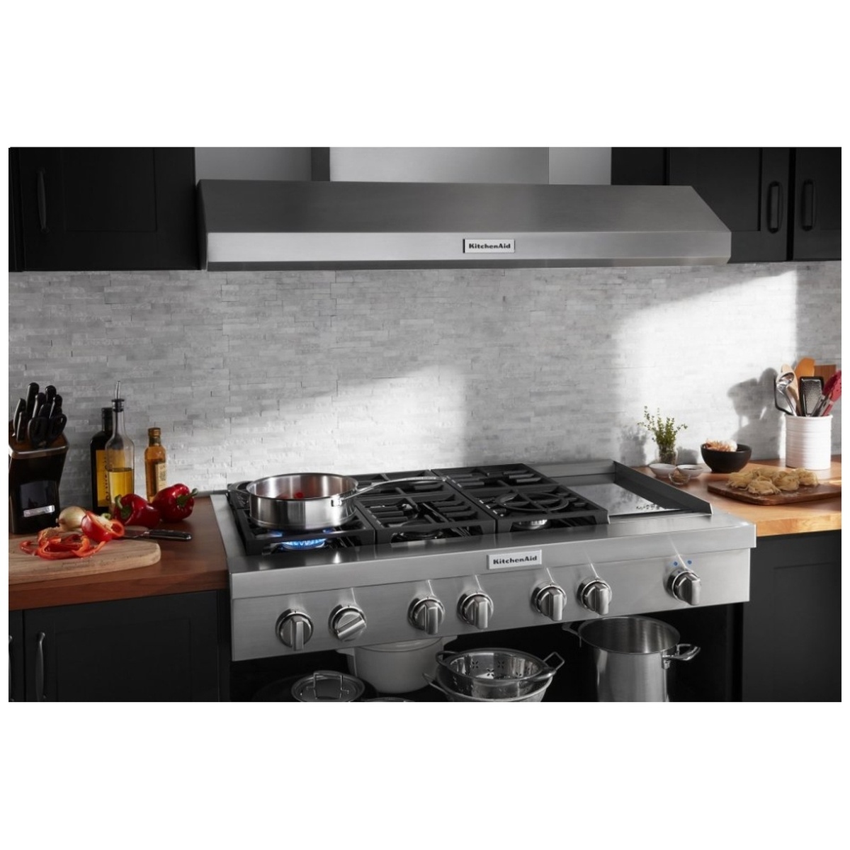 Kitchen installation photo showing a KitchenAid commercial-style rangetop with front knobs and an overhead hood