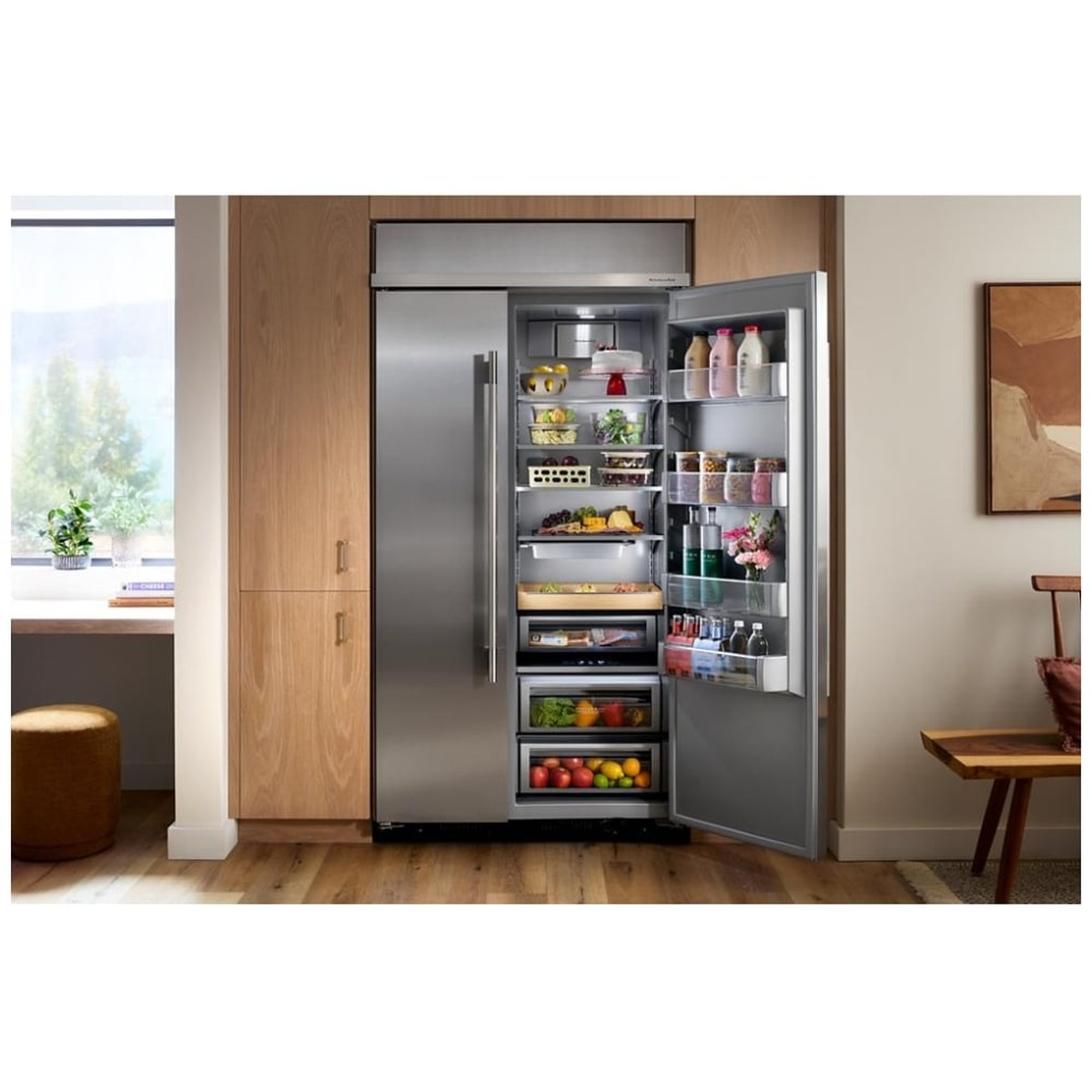 KitchenAid KBSN742SPS installed flush in a warm custom wood-panel kitchen with the refrigerator door open revealing fully stocked organized shelves and door bins