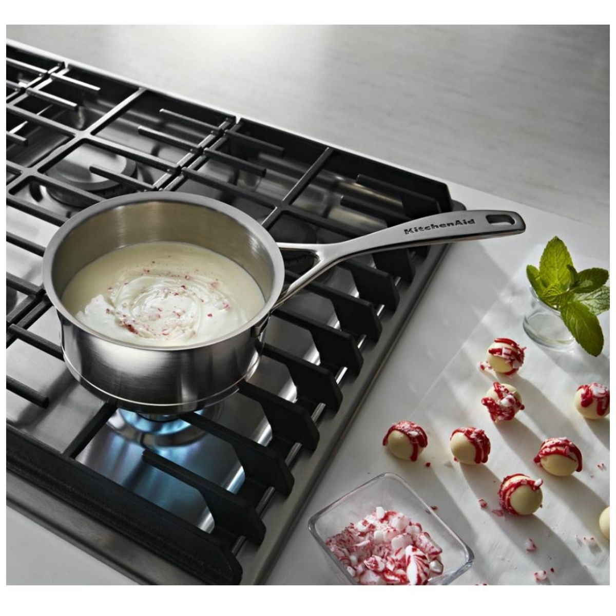 Saucepan heating on a KitchenAid gas cooktop with cast-iron grates in a bright kitchen setting