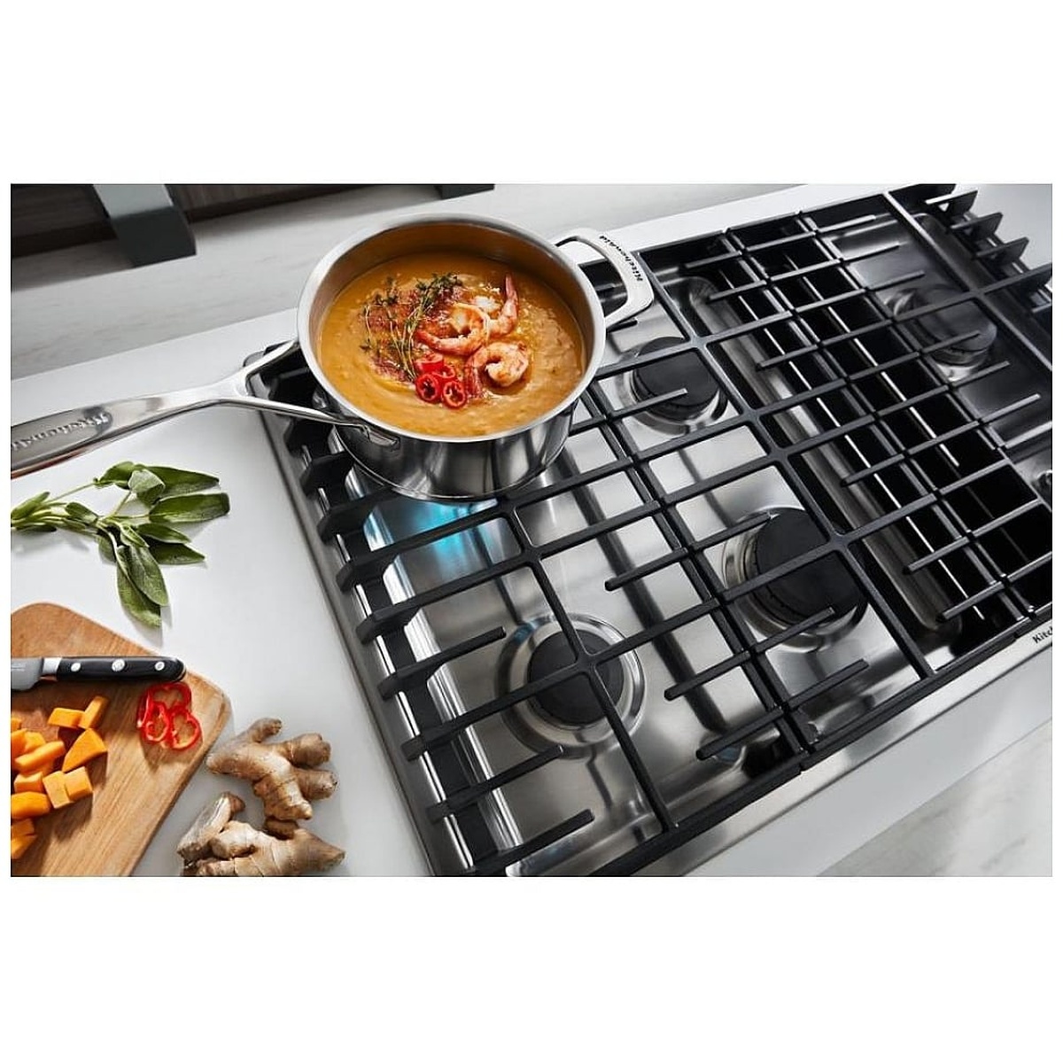 Angled view of a KitchenAid gas cooktop in a kitchen setting with a pot cooking on the cast-iron grates