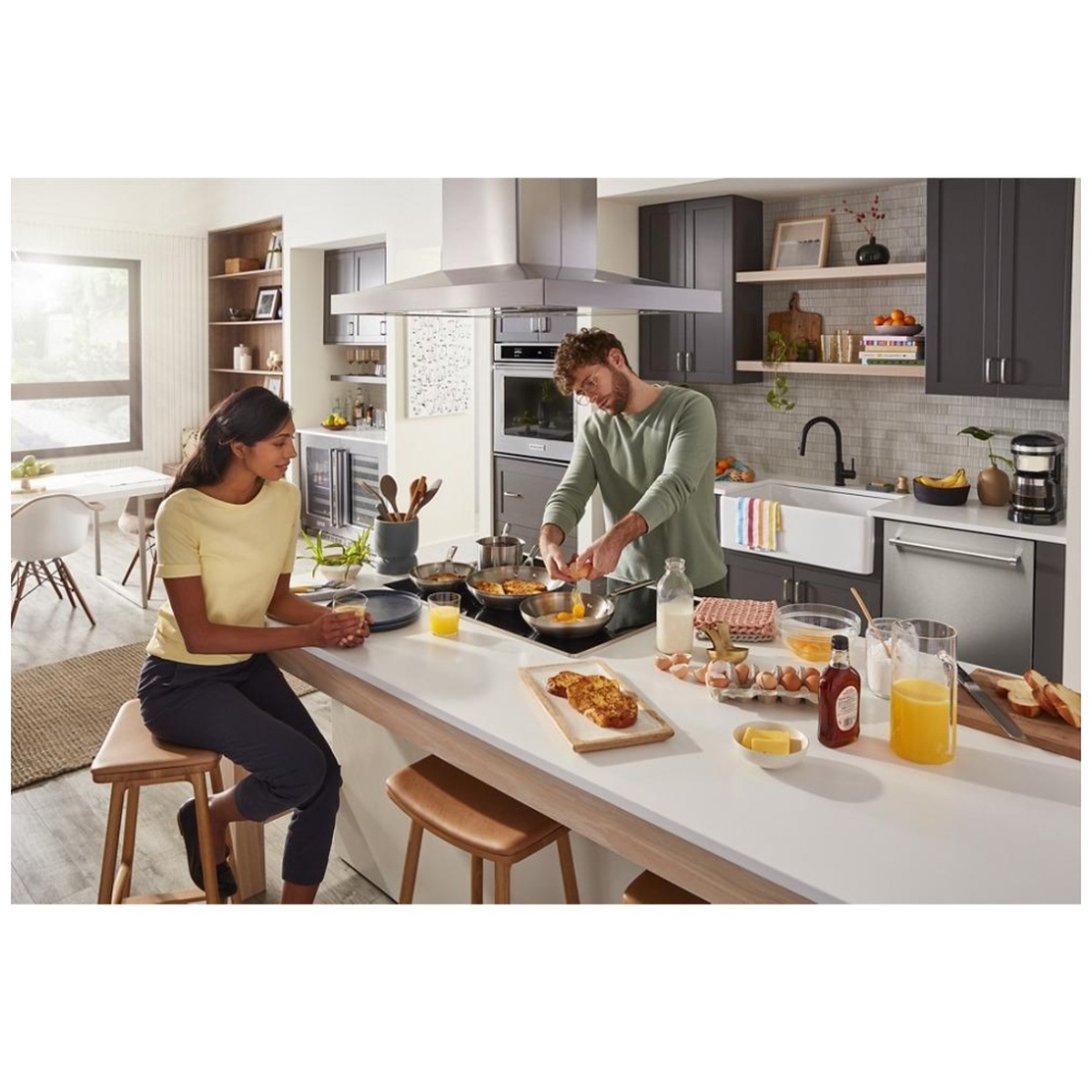 Couple cooking together on a KitchenAid induction cooktop installed in a modern open-concept kitchen with a range hood above