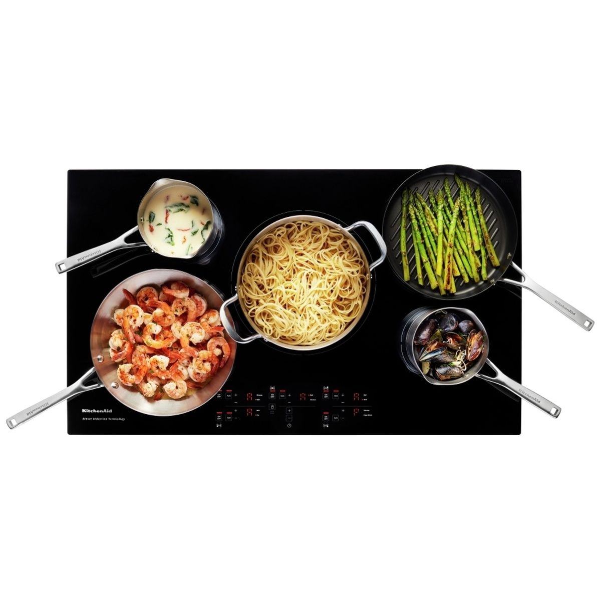 KitchenAid KCIG556JBL cooktop viewed from above with five pans cooking shrimp, pasta, asparagus, mussels and a cream sauce simultaneously across all elements