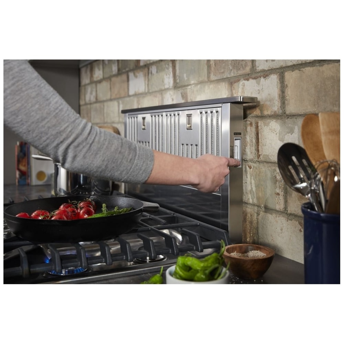 Person pressing the hidden push-button control on the side panel of the KitchenAid KXD4630YSS downdraft unit while cooking on a gas cooktop
