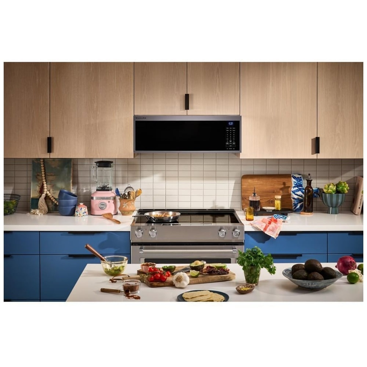 KitchenAid YKMML550RPS low-profile over-the-range microwave installed above a range in a modern kitchen with blue cabinetry and wood upper cabinets