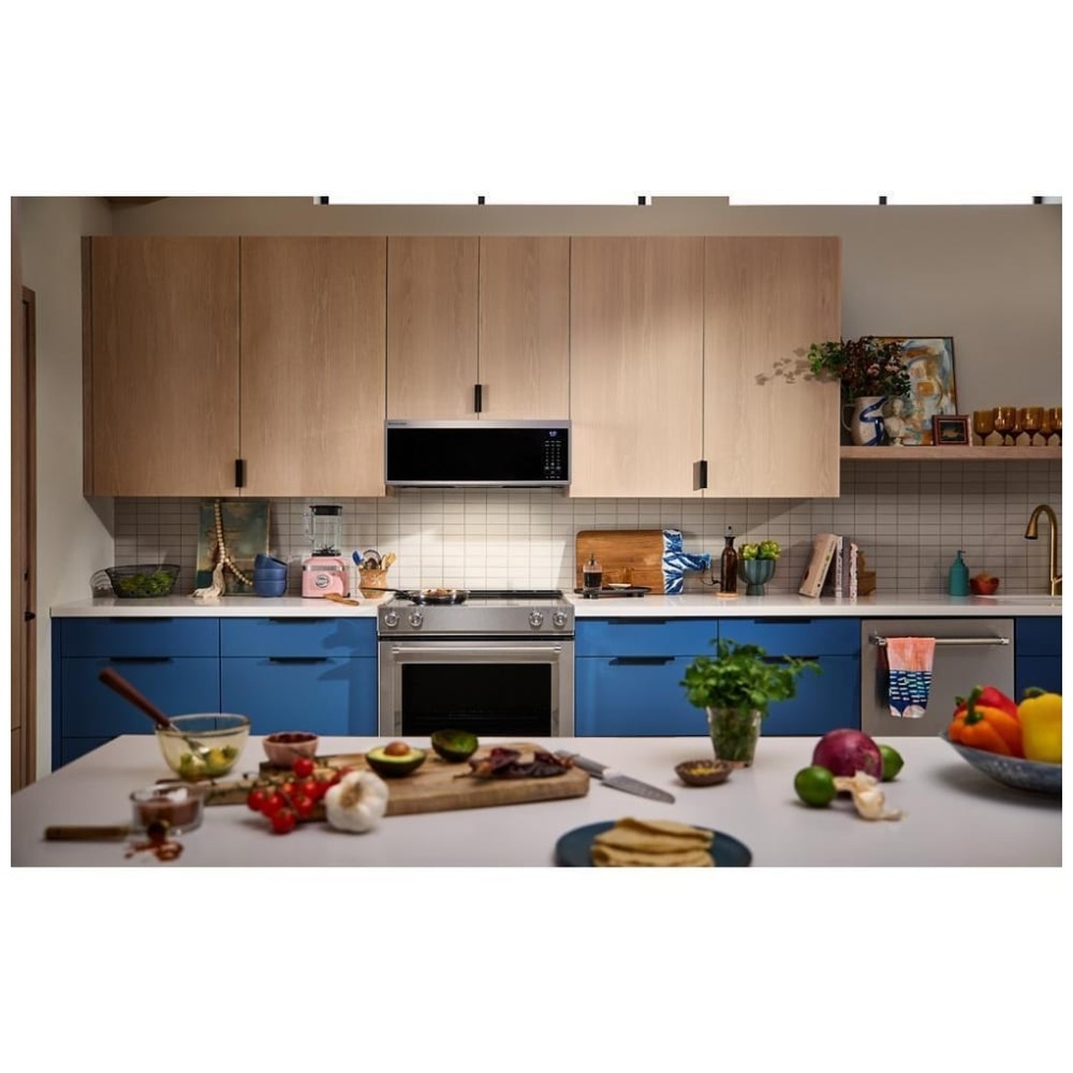 KitchenAid low-profile over-the-range microwave viewed from across a kitchen island in a styled space with blue and wood cabinetry, produce on the counter