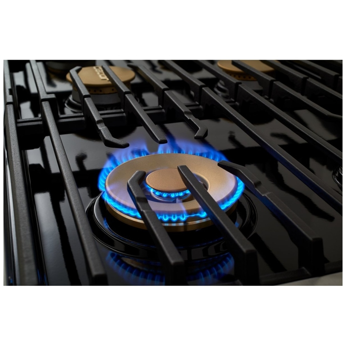 Close-up of Dacor DOP36P86GLS dual-ring brass burner lit with blue flame, surrounded by continuous cast-iron grates on the gas cooktop