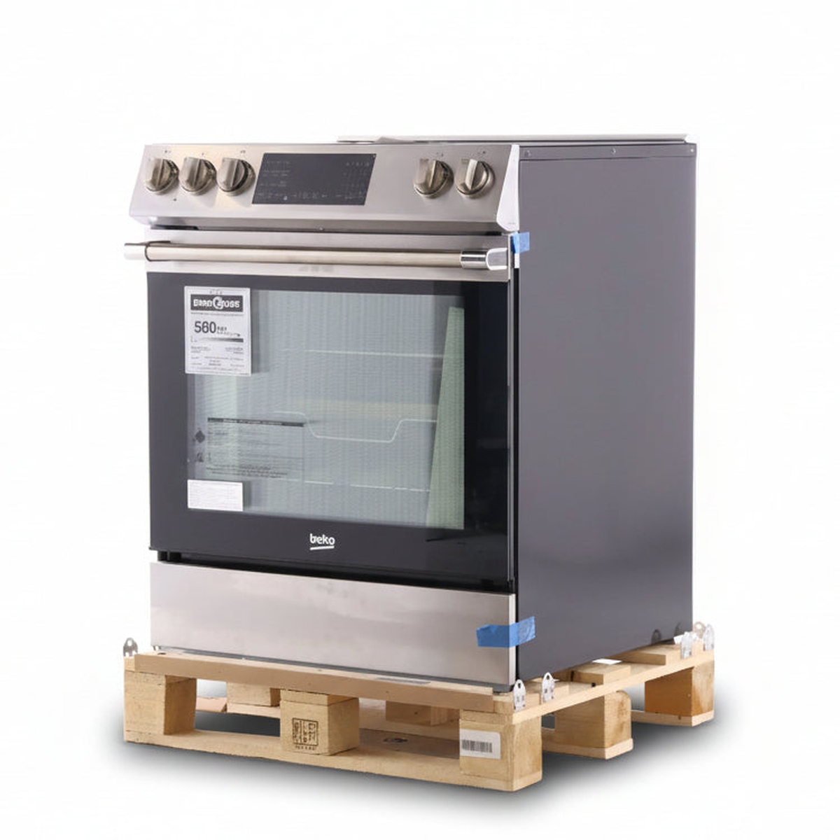 Angled view of a Beko stainless slide-in electric range on a wooden pallet, showing the front control panel, oven door window, and side panel.