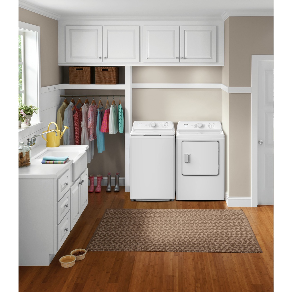 Frigidaire washer and dryer pair installed in a bright, organized laundry room with overhead cabinets, hanging clothes, and hardwood floors