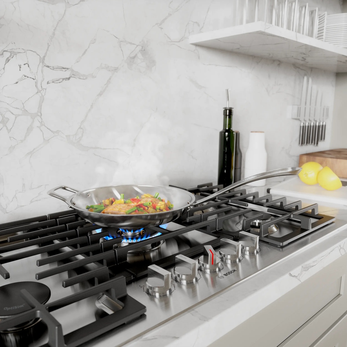 Lifestyle shot of the Bosch NGM8658UC gas cooktop installed in a modern white marble kitchen with a stainless steel pan cooking fish and vegetables over an active blue gas flame