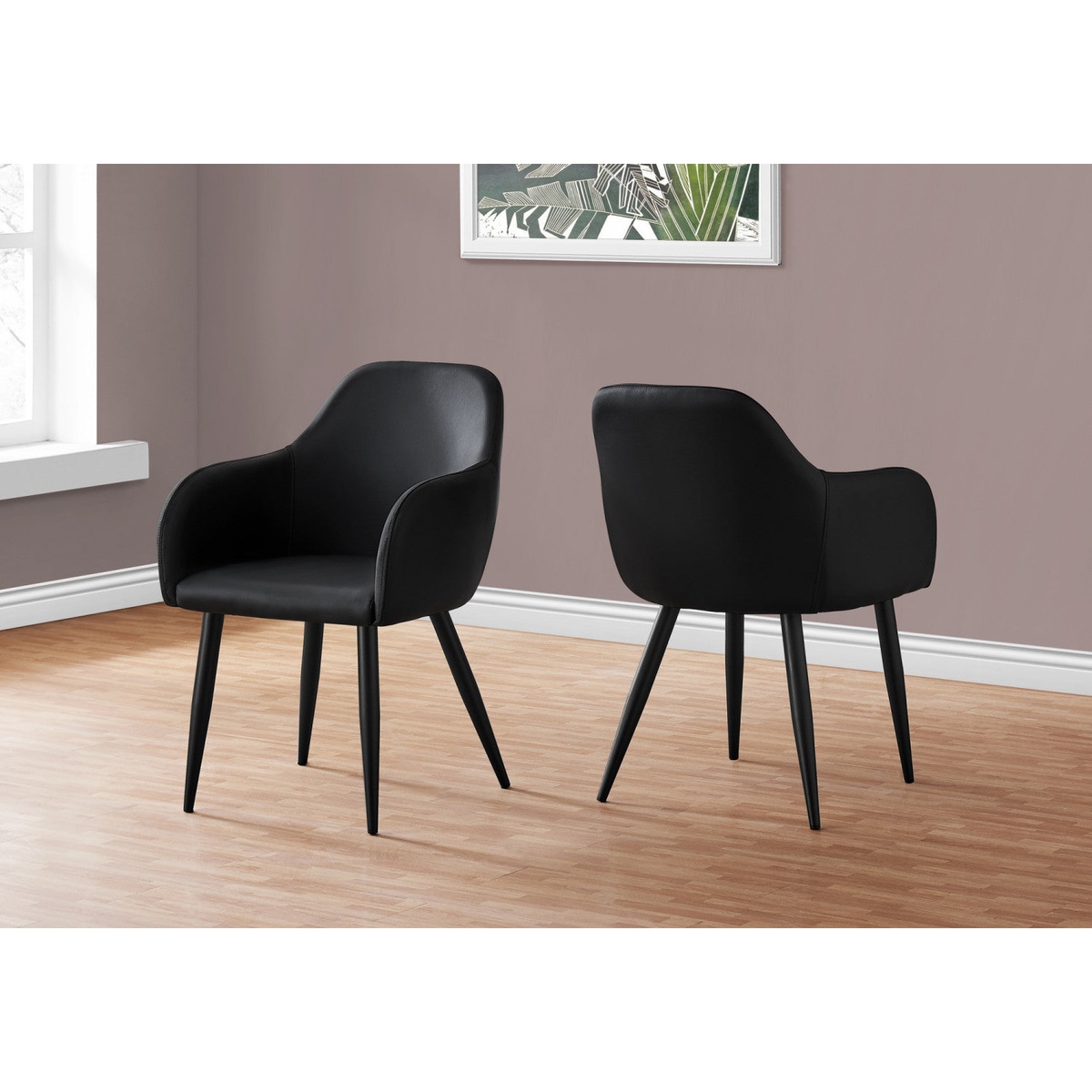 Two black leather-look Amara dining chairs with integrated armrests and tapered metal legs styled in a modern room with hardwood flooring