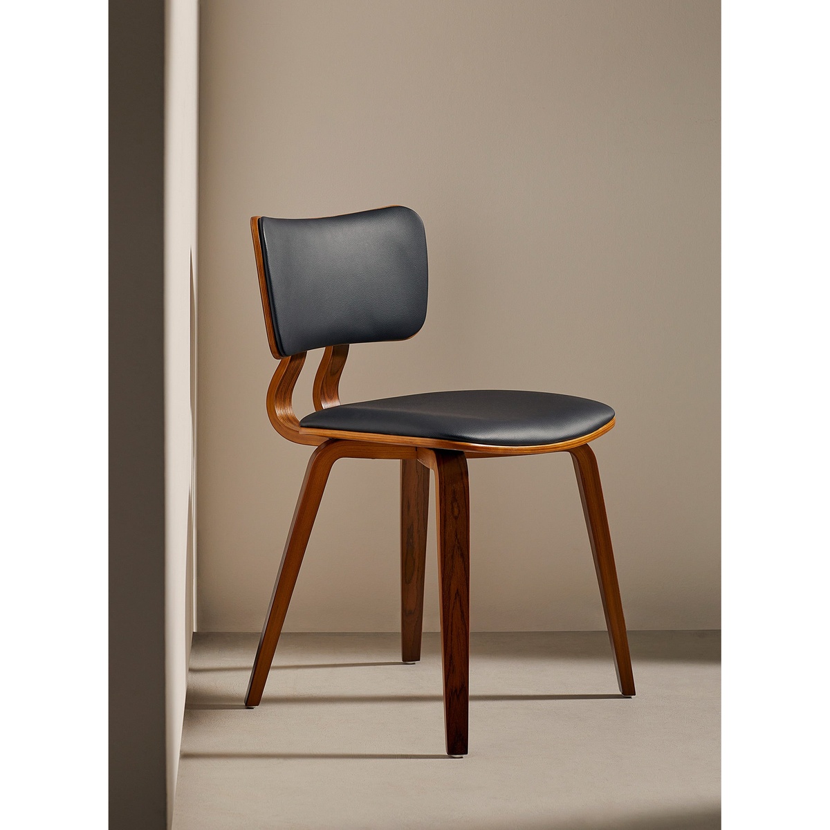 Zaki dining chair with black vegan leather seat and back cushions on a walnut bentwood frame, photographed in a warm, neutral room setting