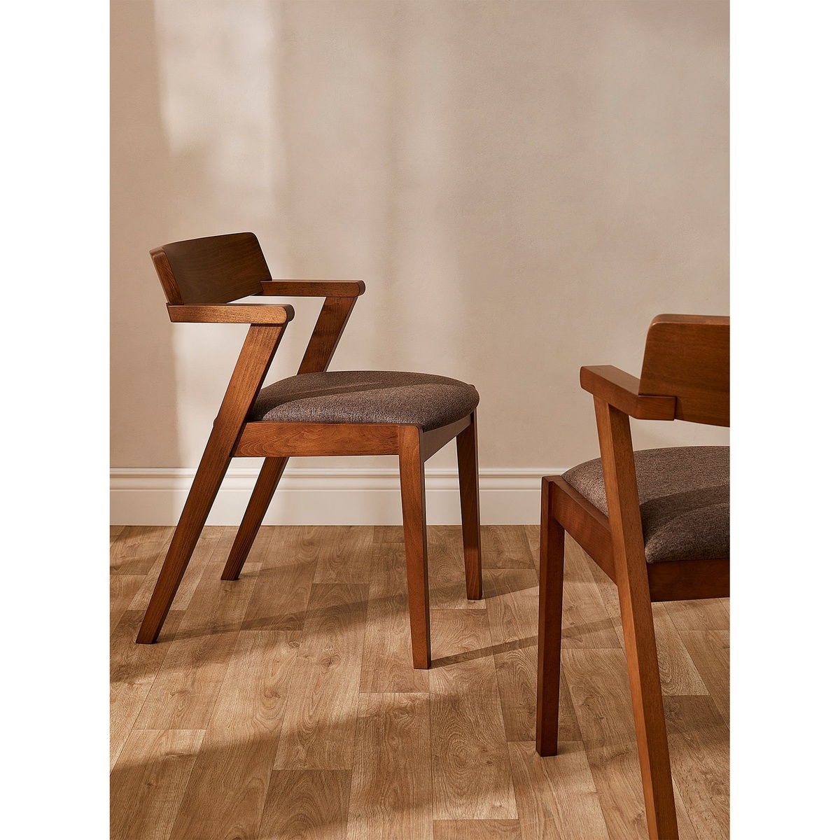 Two Zola dining chairs with solid oak walnut frames and chestnut upholstered seats styled on a light hardwood floor against a warm neutral wall