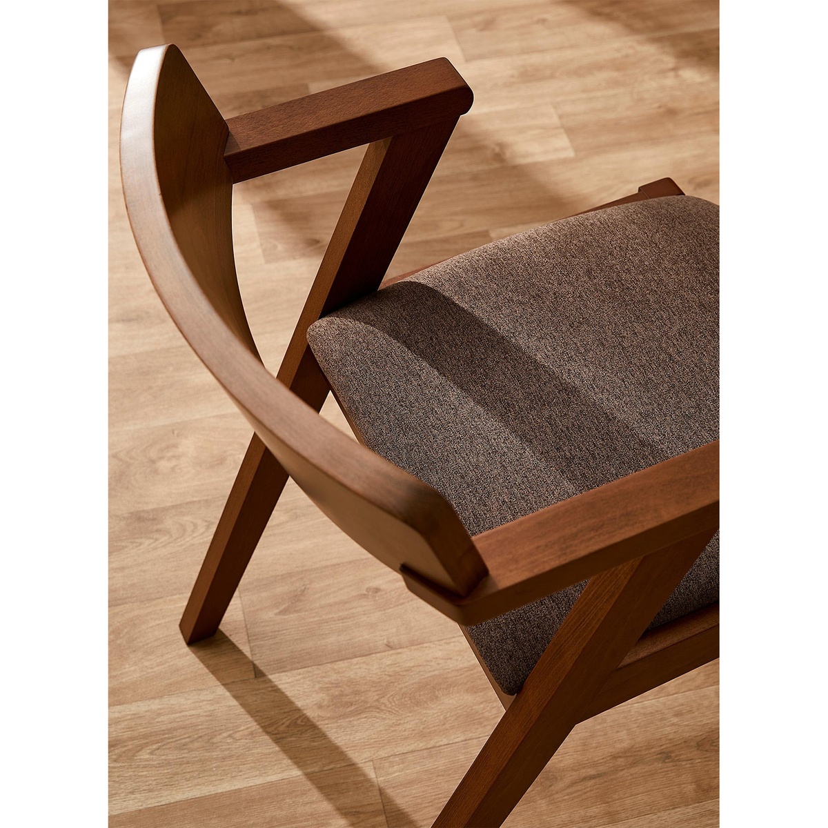 Close-up overhead detail of the Zola chair showing the curved solid oak backrest, angular arm joinery, and chestnut fabric upholstered seat cushion