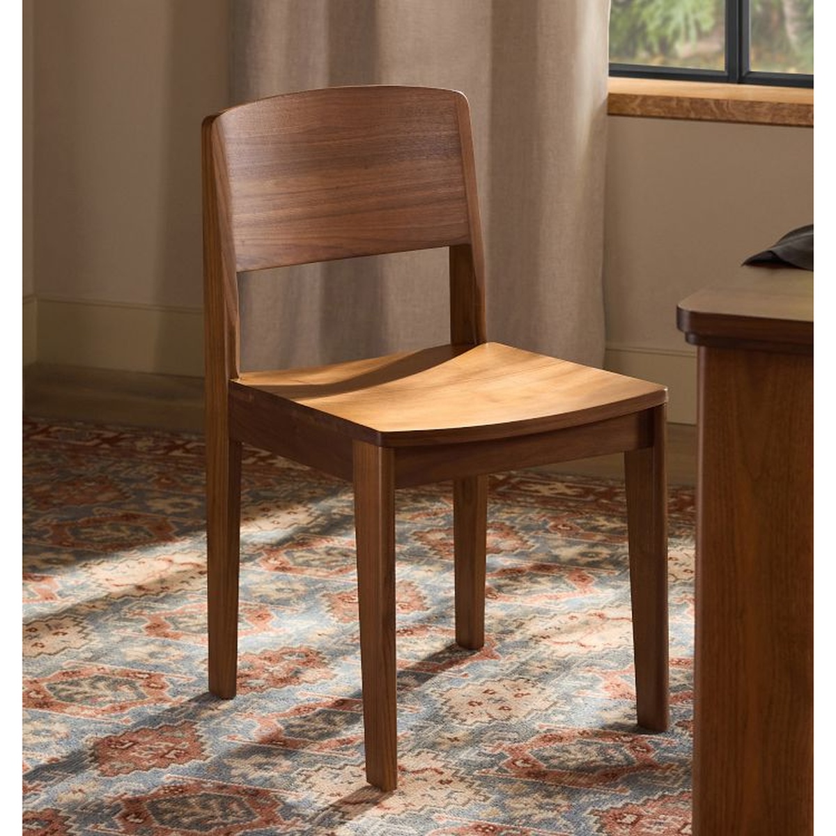 Anders Dining Chair in walnut shown in a warm, naturally lit dining room beside a wood table and a patterned area rug