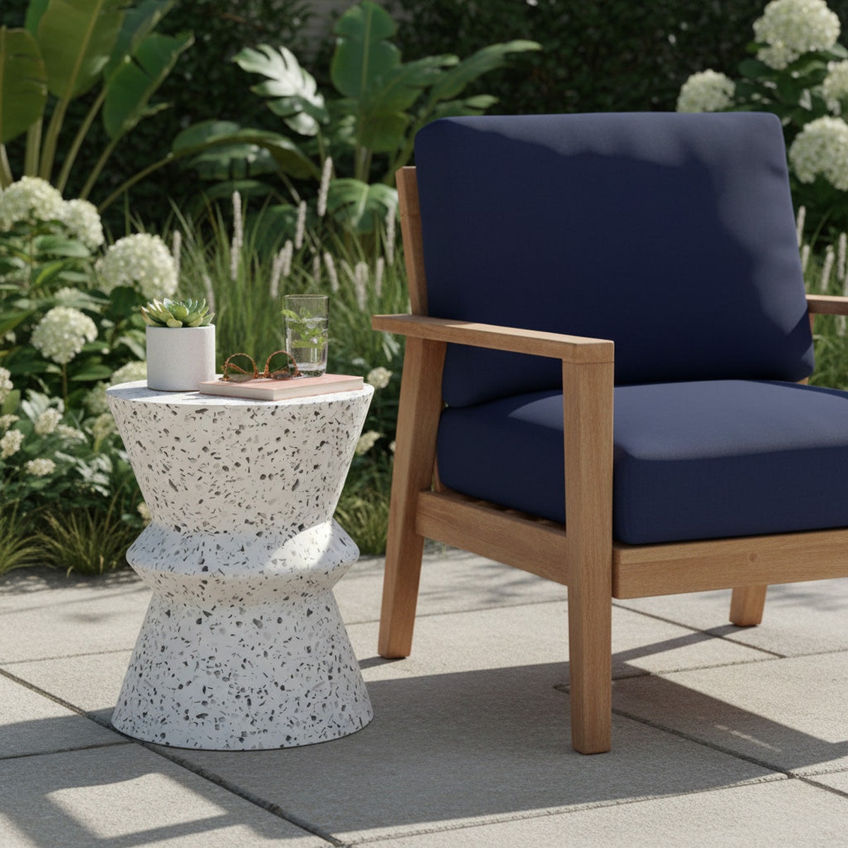 Terrazzo hourglass side table used outdoors beside a wood-framed lounge chair, holding a plant, glasses, and a drink