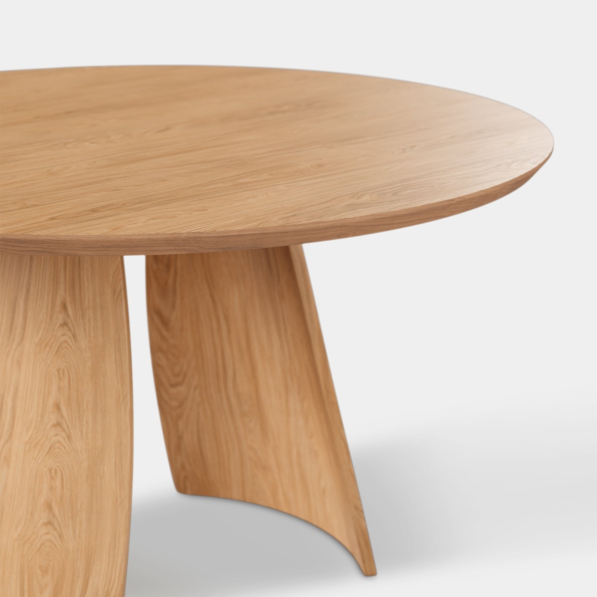 Close-up detail of the Obelia Oak dining table showing the smooth round tabletop edge and the curved sculptural base panels in natural oak veneer