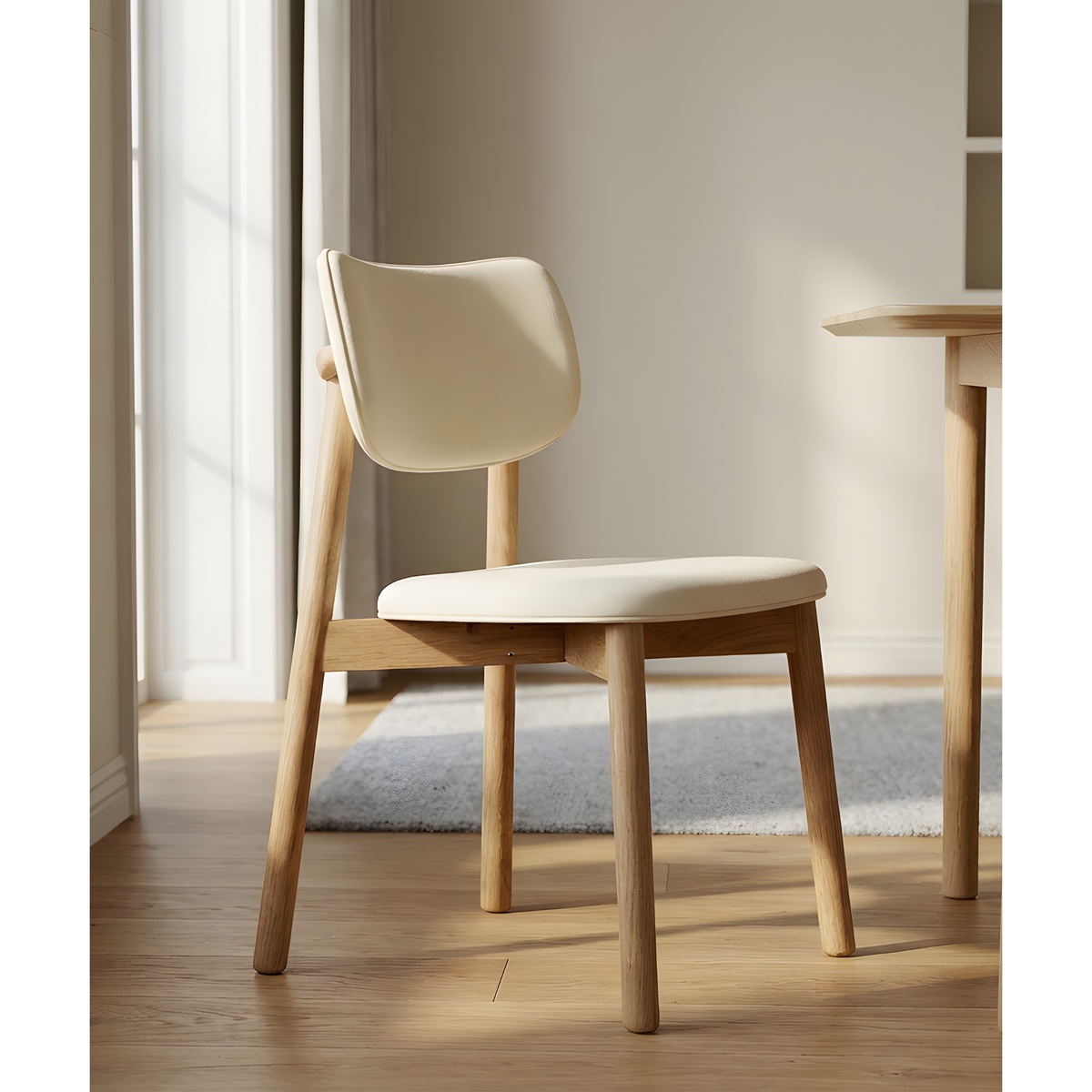 Side view of a beige upholstered dining chair with an oak wood frame next to a dining table in a bright room
