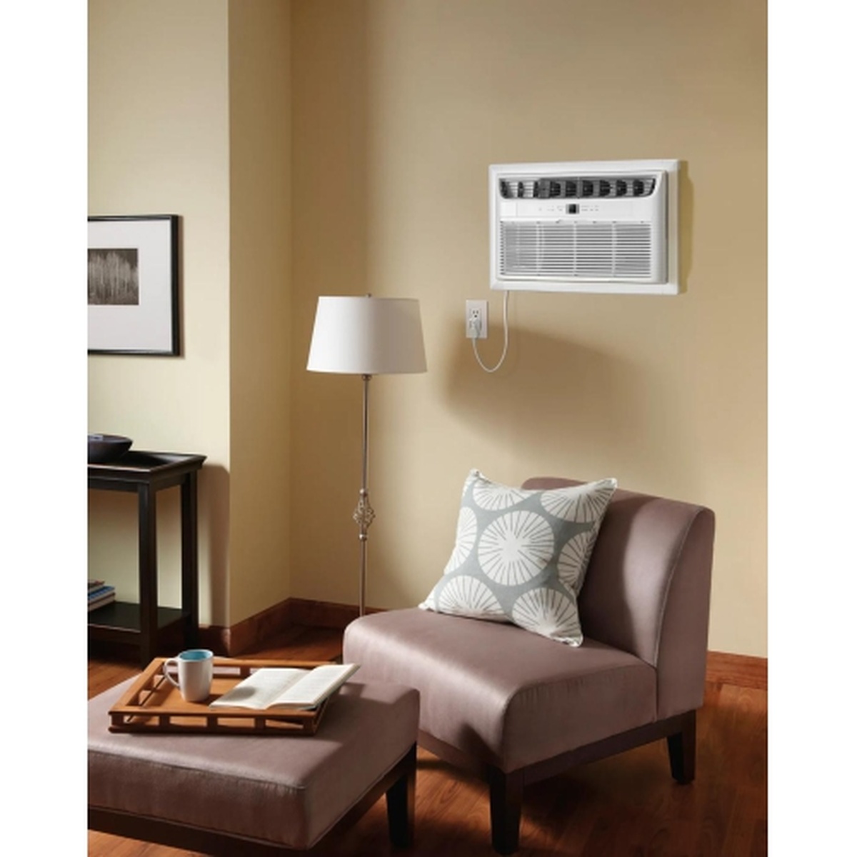 Frigidaire through-the-wall air conditioner installed flush in a living room wall above a couch, showing a clean in-wall mounted look in a warmly lit room