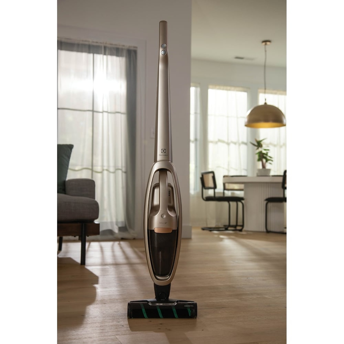 Electrolux WellQ7 cordless stick vacuum standing upright on a hardwood living room floor with the PowerPro Roller nozzle visible at the base