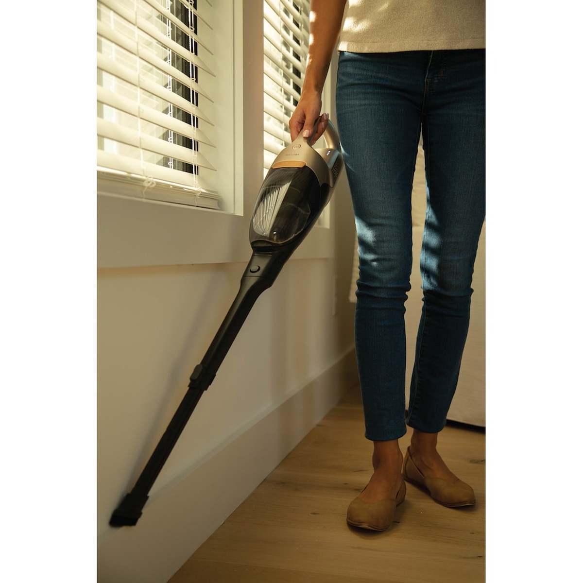 Person holding the detached Electrolux WellQ7 hand unit with the extension wand attached, cleaning near a window baseboard on a hard floor