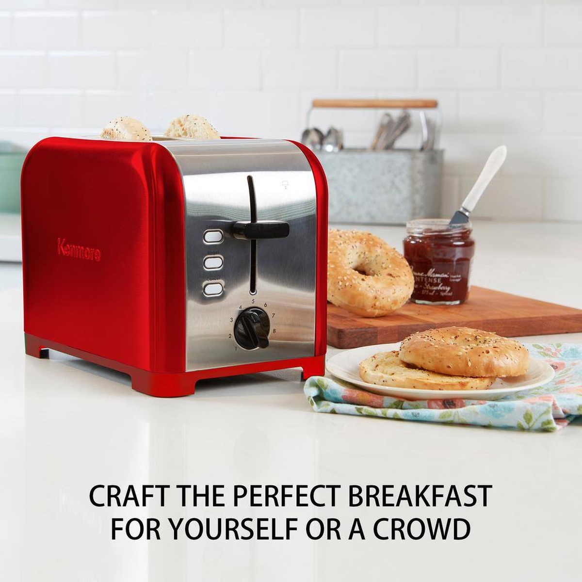 Kenmore red and stainless toaster on a kitchen counter next to bagels, jam, and a plate