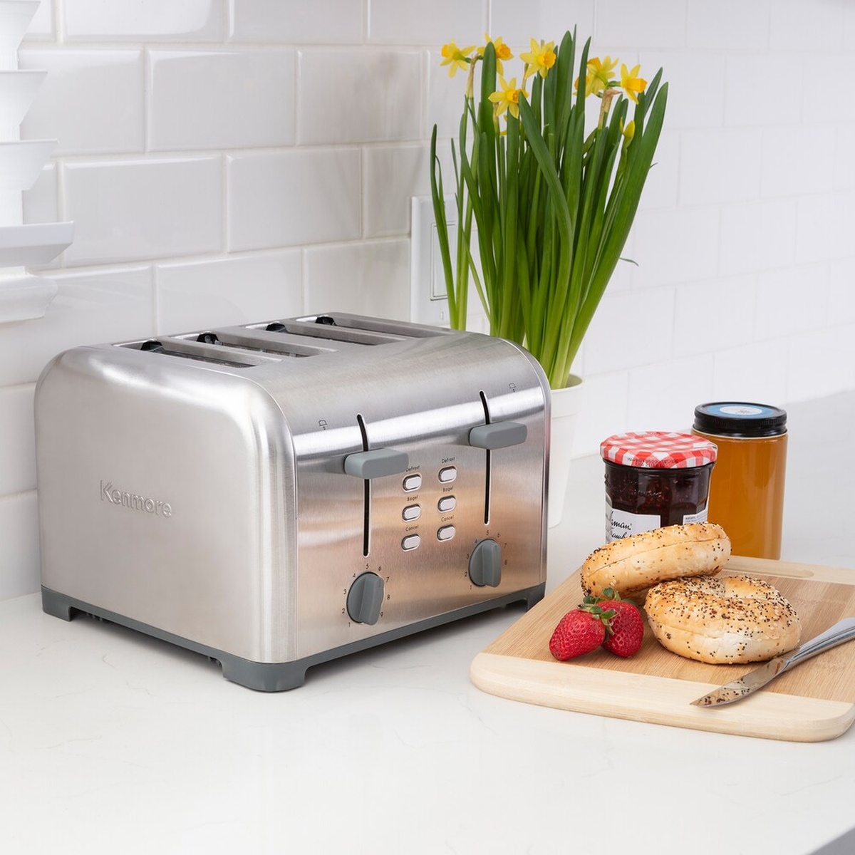 Kenmore stainless steel 4-slice toaster on a kitchen counter next to bagels, jam, and flowers