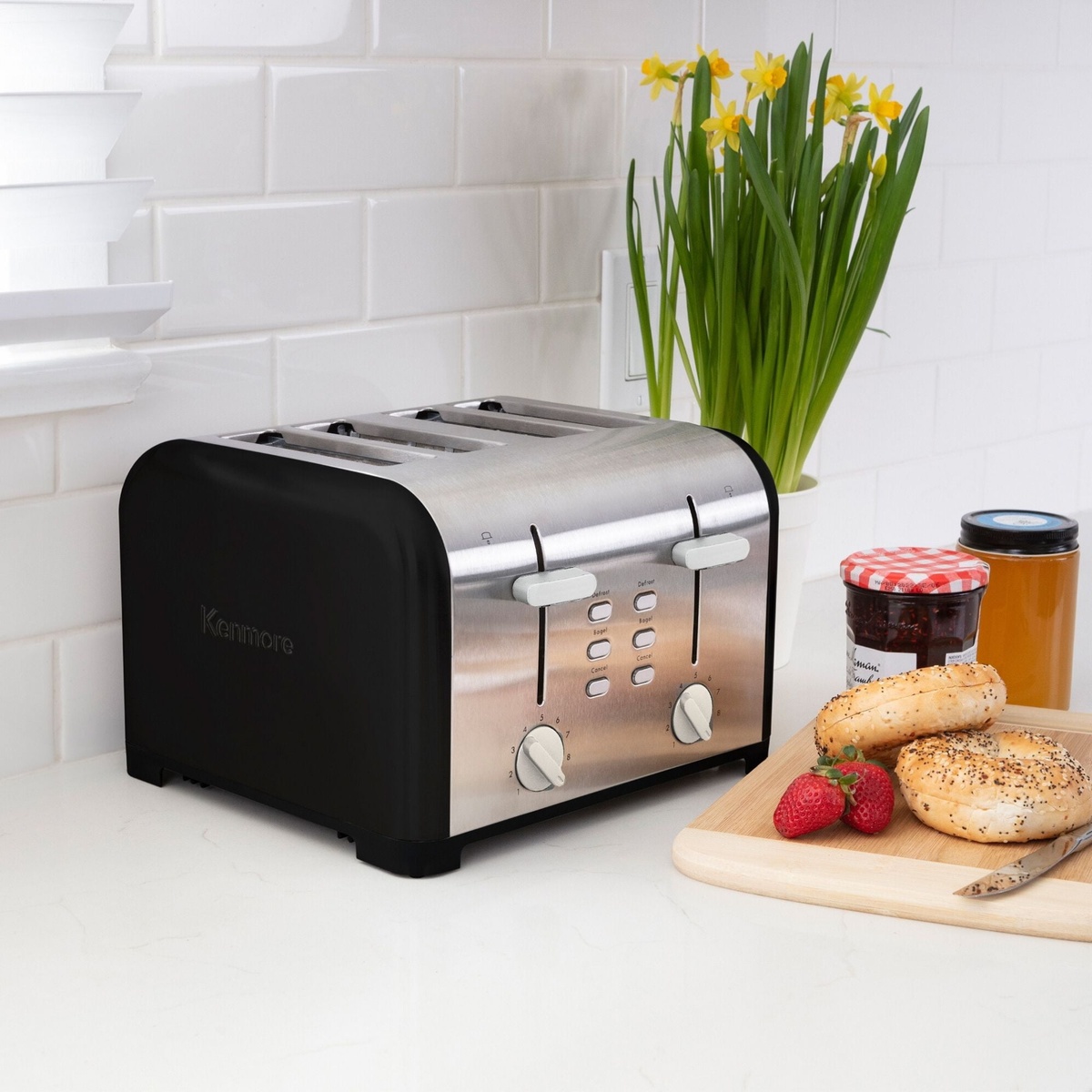 Kenmore 4-slice toaster on a kitchen counter beside bagels, jam jars, and flowers