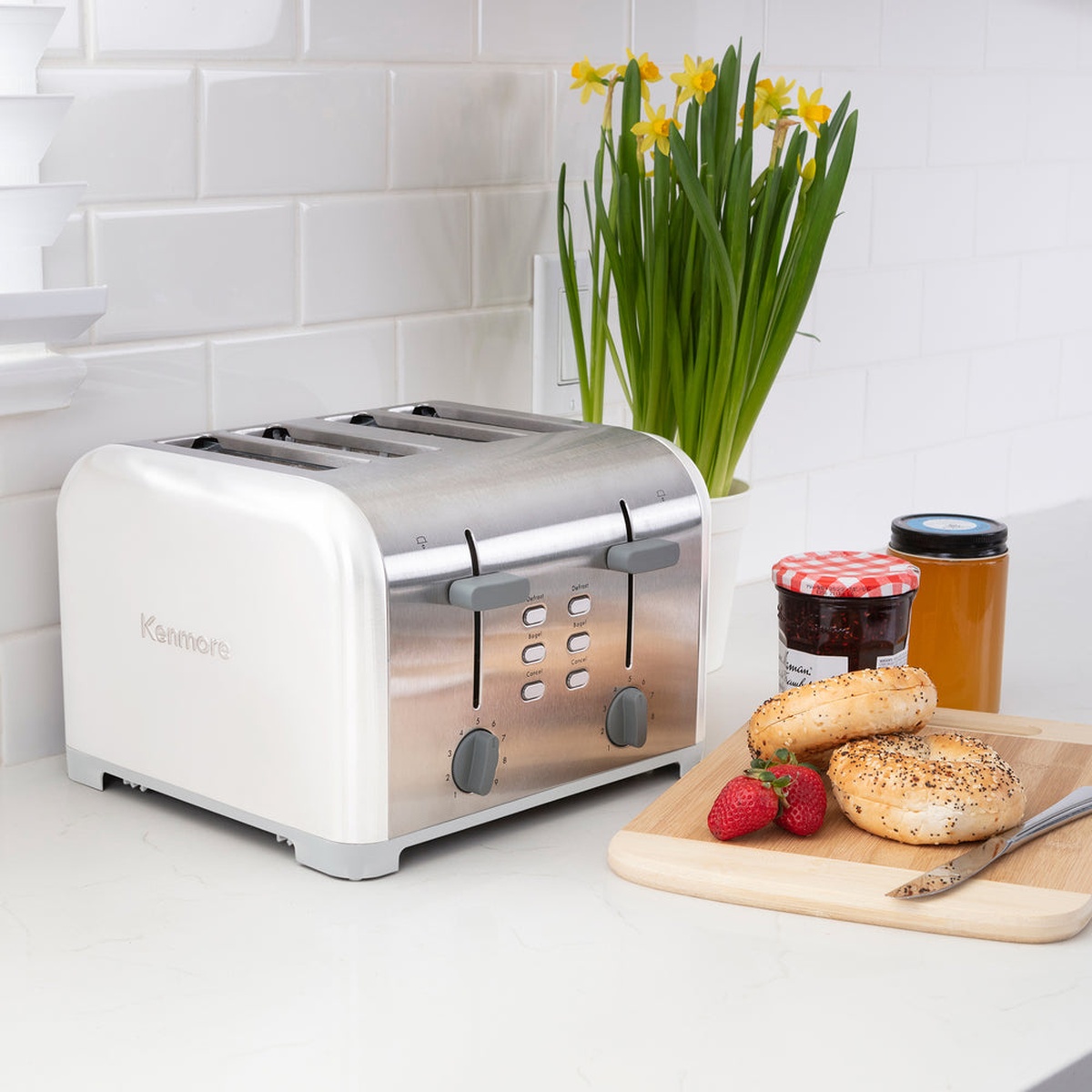 Kenmore 4-slice toaster on a kitchen counter beside bagels, jam jars, and flowers