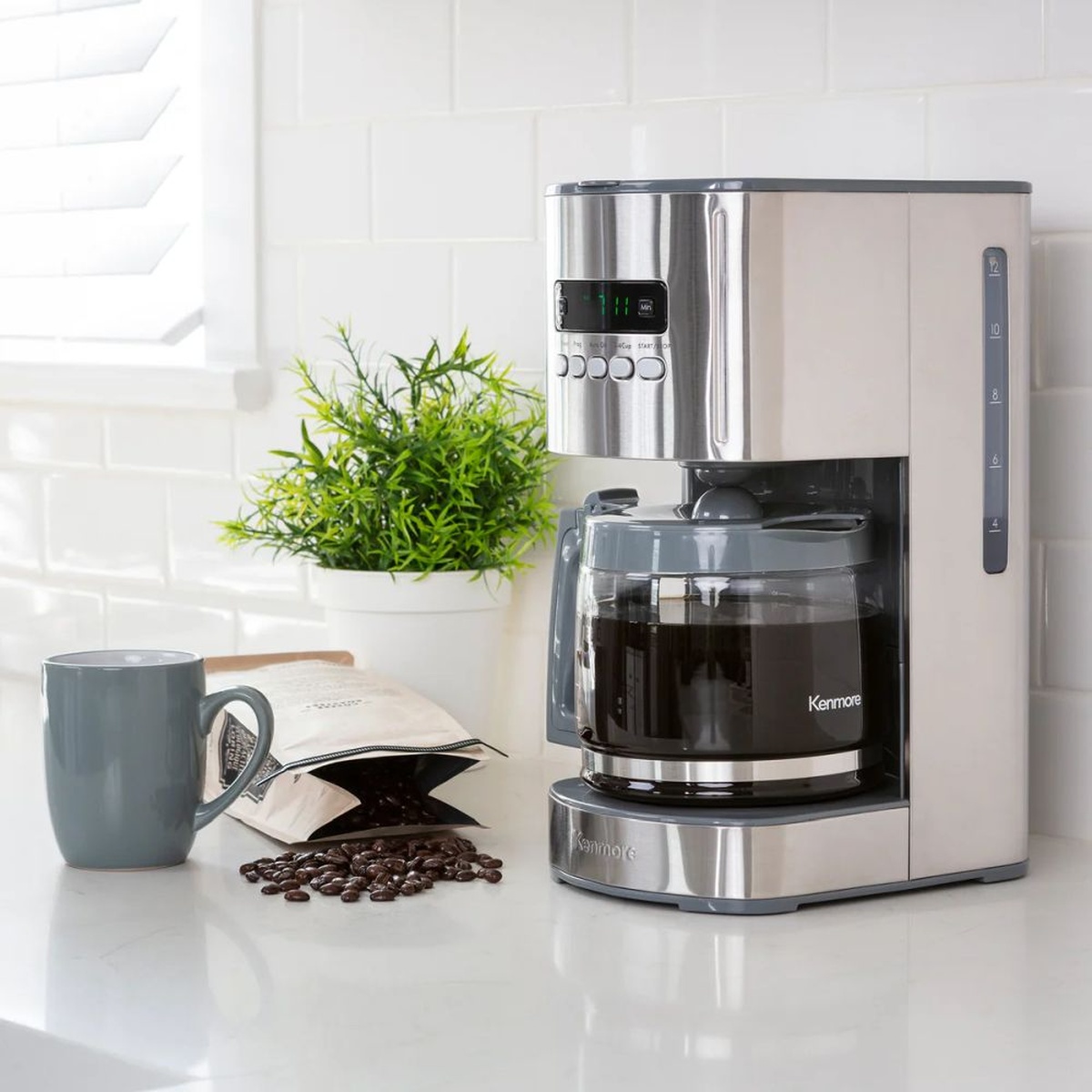 Kenmore drip coffee maker on a bright kitchen counter next to a mug and coffee beans