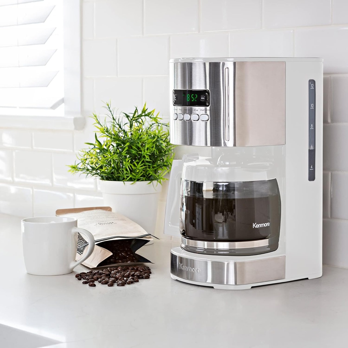 Kenmore white drip coffee maker with stainless accents on a kitchen counter beside a mug and coffee beans