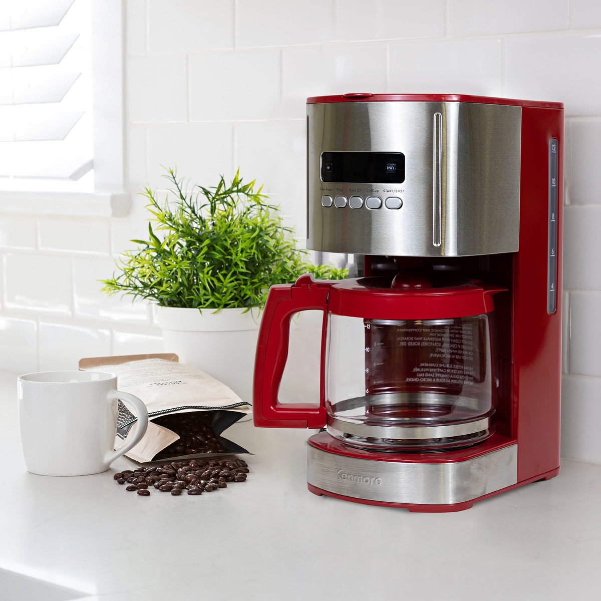 Kenmore red and stainless coffee maker on a kitchen counter next to a mug, coffee beans, and a bag of coffee