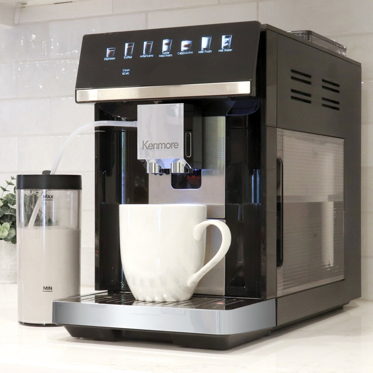 Kenmore super automatic espresso machine on a kitchen counter dispensing coffee into a mug, with a milk container connected by a tube