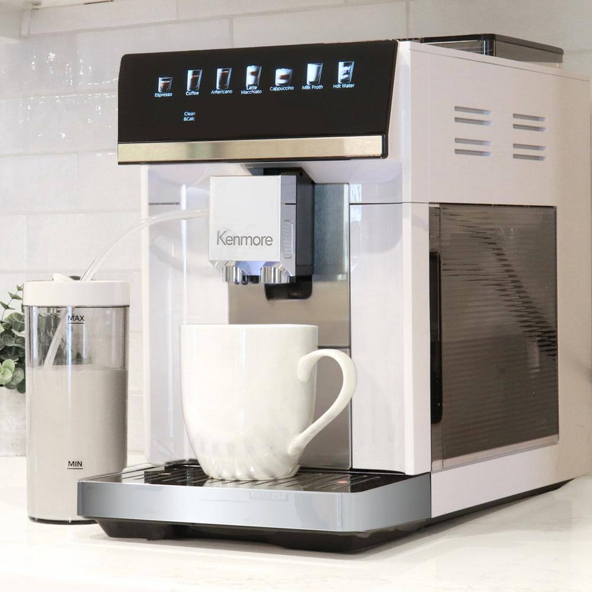 Kenmore super automatic coffee machine on a kitchen counter with a cup under the spout and a milk container connected