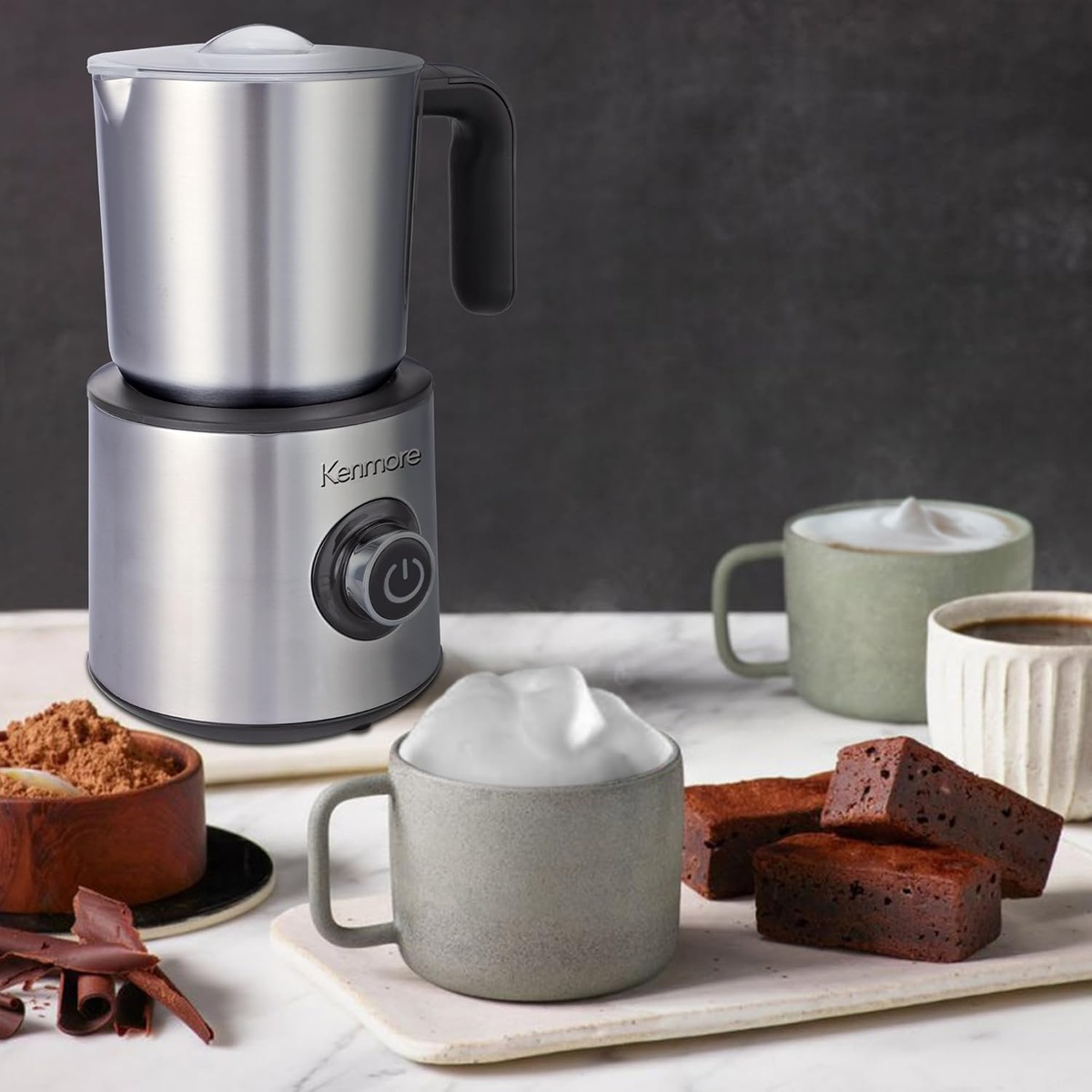 Kenmore milk frother on a countertop beside mugs of coffee drinks and dessert