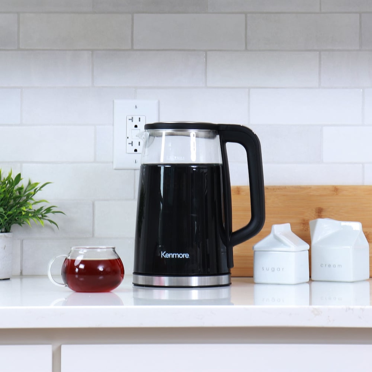 Kenmore electric kettle staged on a kitchen counter beside a glass cup of tea