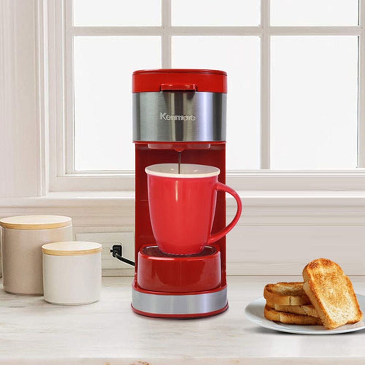 Red Kenmore single-serve coffee maker on a kitchen counter brewing into a red mug