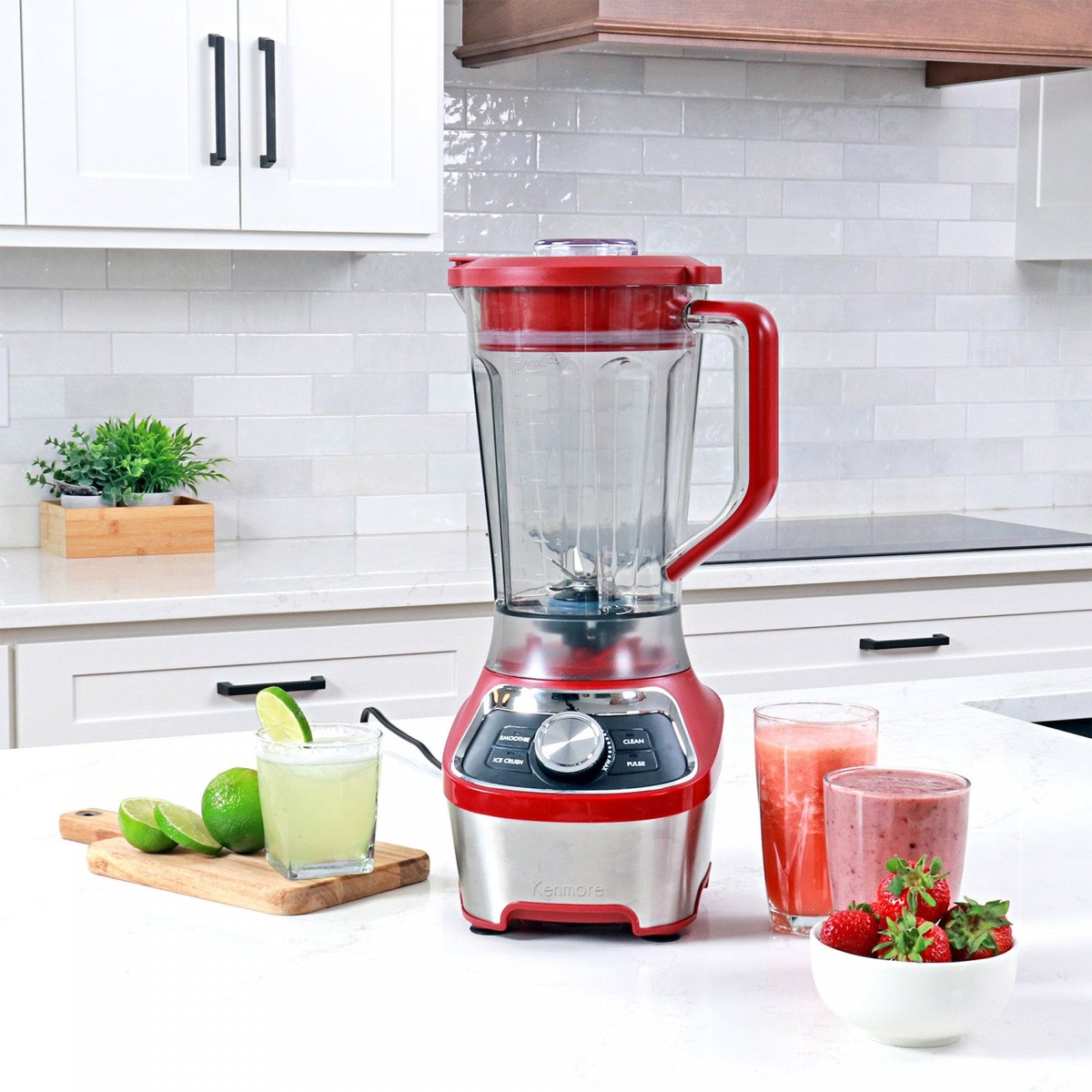Kenmore red stand blender on a kitchen counter with prepared drinks and fruit nearby