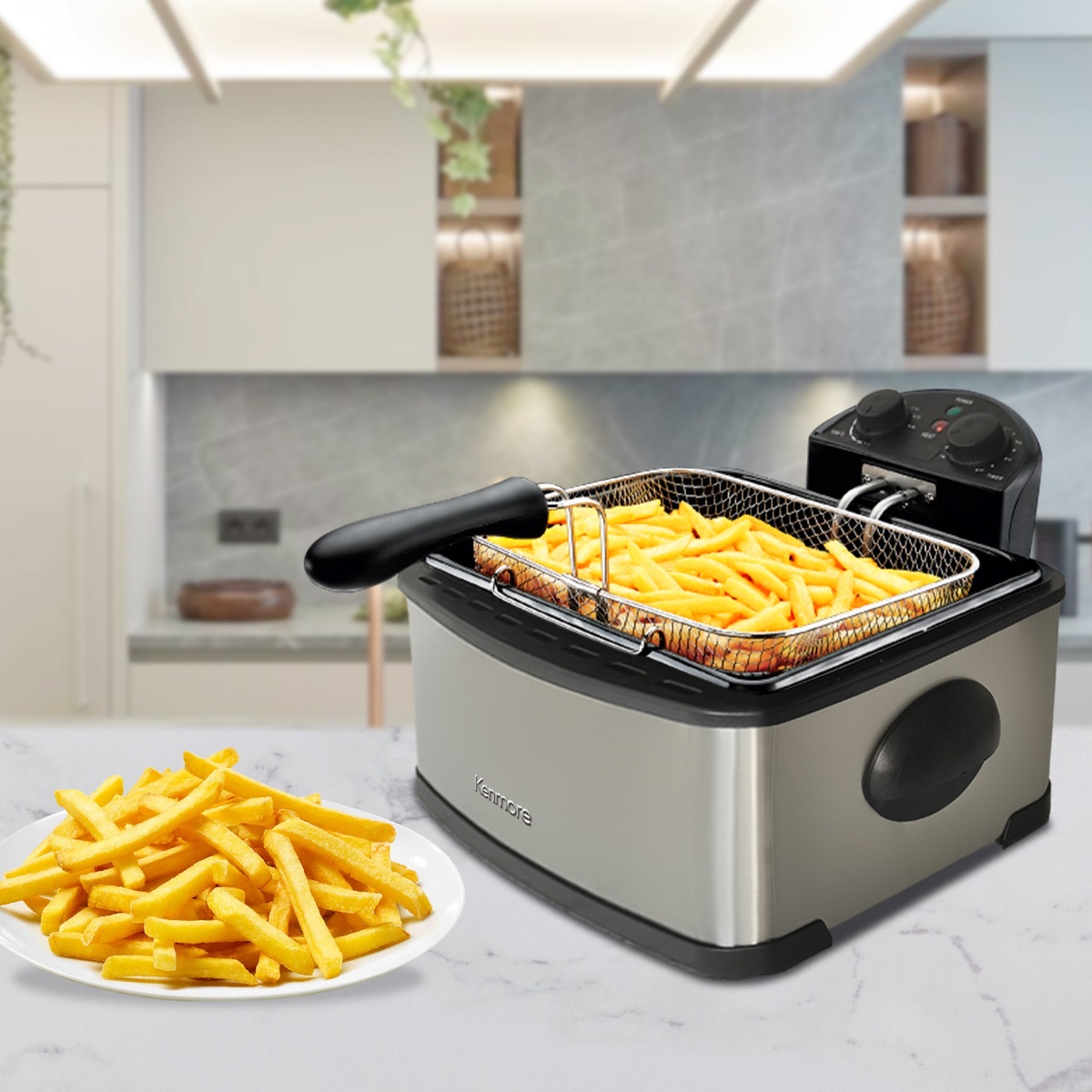 Kenmore stainless steel deep fryer on a kitchen counter with a basket of fries and a plate of cooked fries