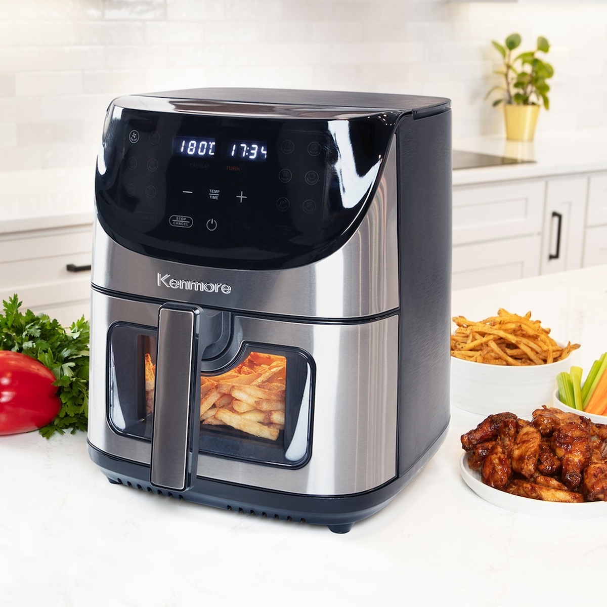 Kenmore stainless-steel air fryer on a kitchen counter with fries visible through the front window and plated food nearby