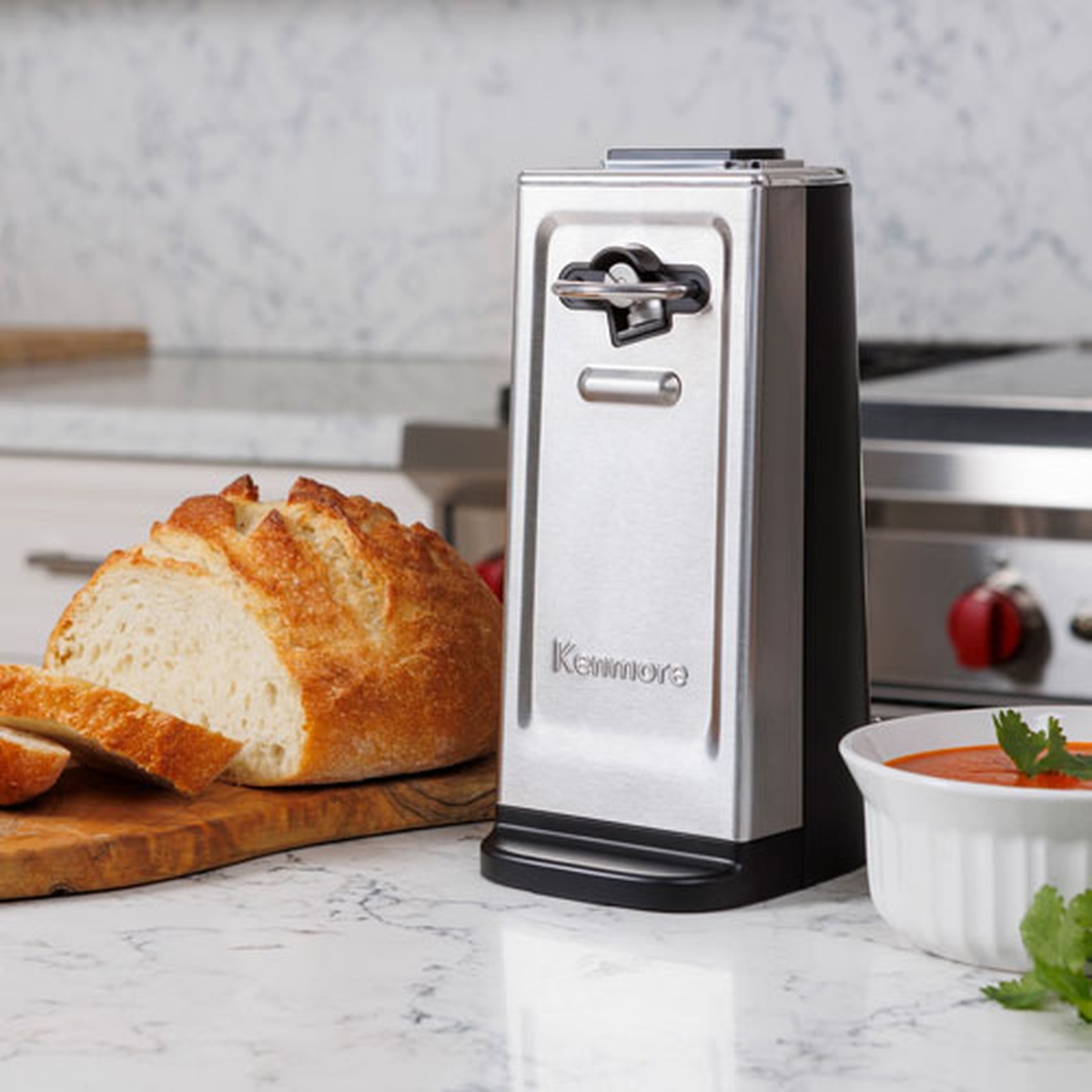 Kenmore stainless steel electric can opener on a kitchen counter beside bread and a bowl