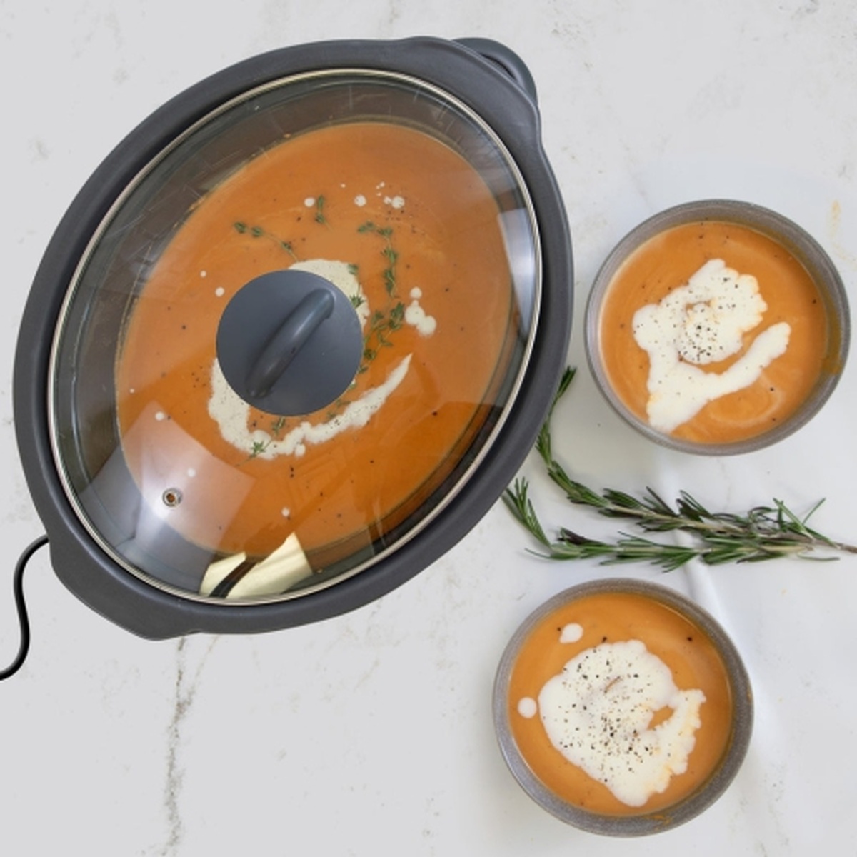 Top view of a slow cooker filled with soup on a countertop beside two bowls of soup