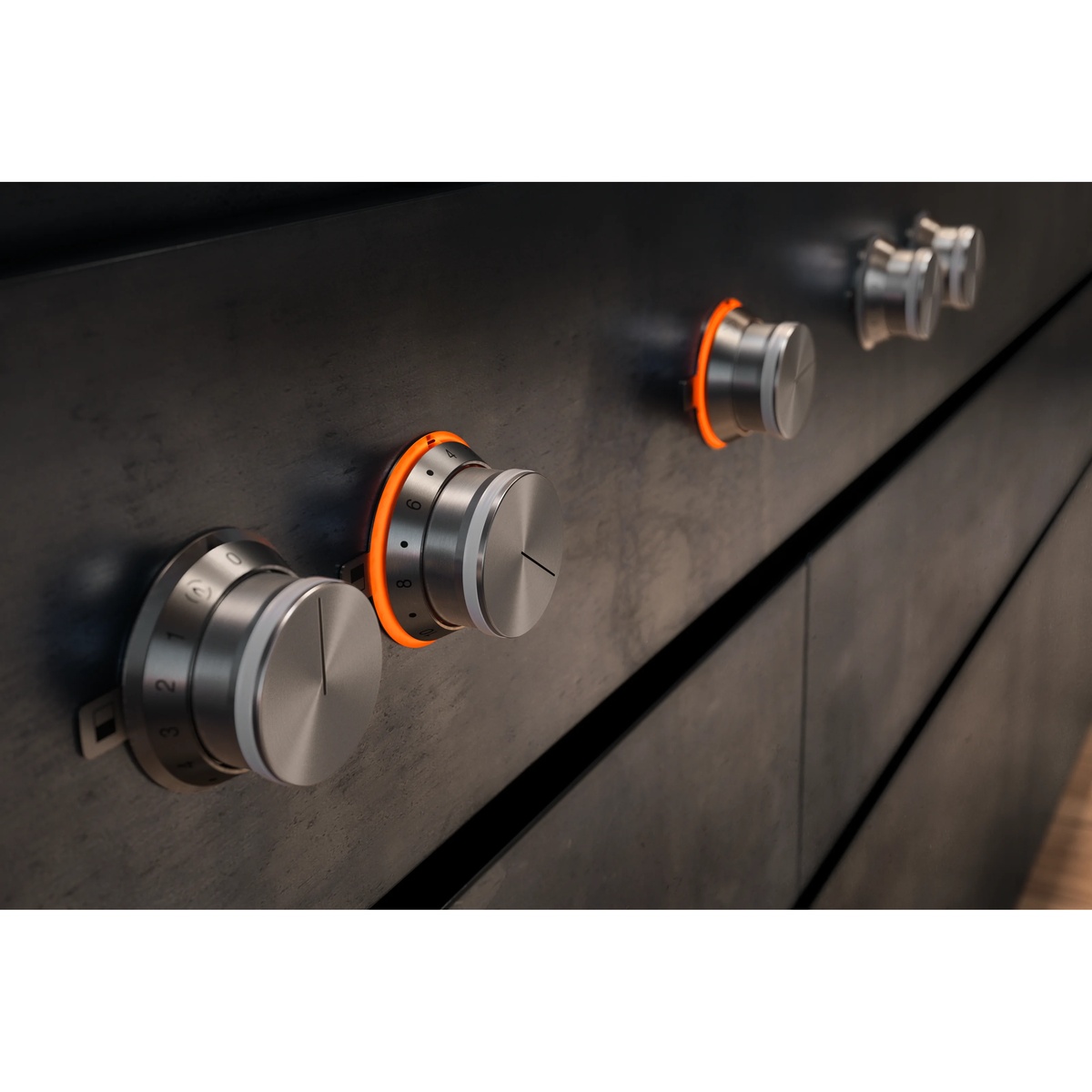 Close-up of Gaggenau stainless steel rotary knobs with glowing orange illuminated rings mounted on a dark cooktop surface, showing numbered heat level dial markings