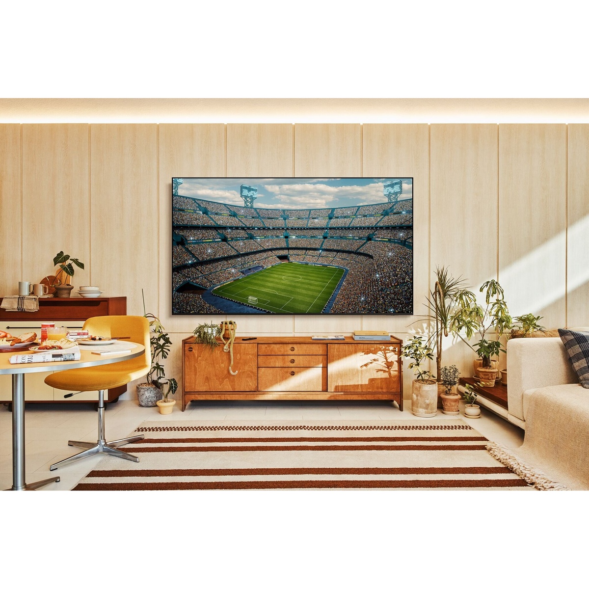 Samsung Crystal UHD TV wall-mounted in a warm modern living room displaying a vivid aerial stadium view