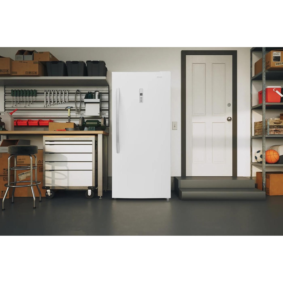 White Frigidaire upright refrigerator placed in a garage setting next to a workbench