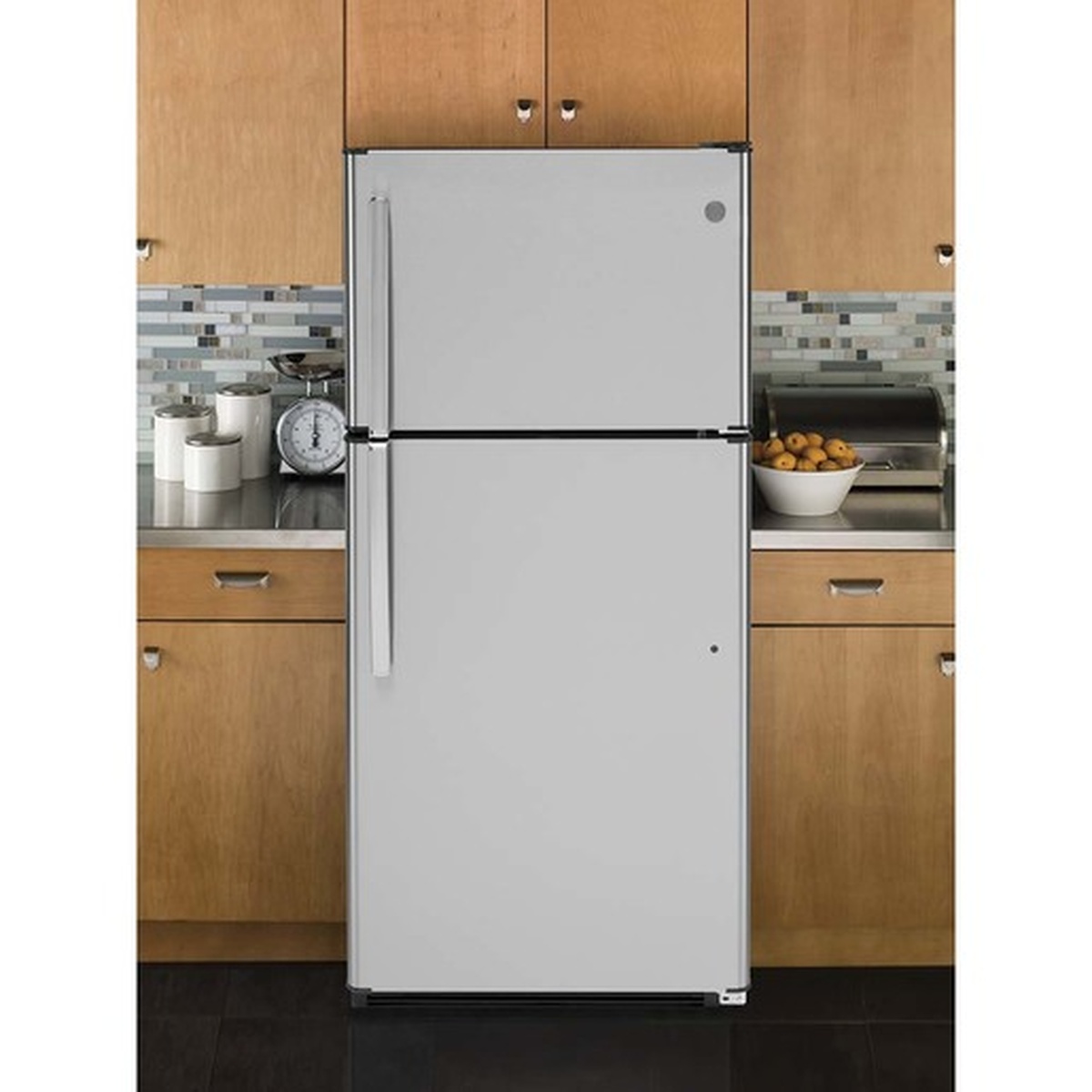 GE stainless steel top-freezer refrigerator installed in a warm wood-tone kitchen with tile backsplash