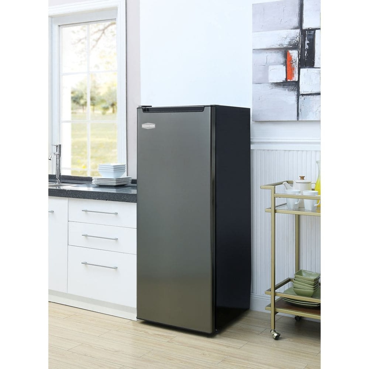 Marathon MUF65BLS black steel upright freezer standing in a bright modern kitchen beside white cabinetry and a gold serving cart