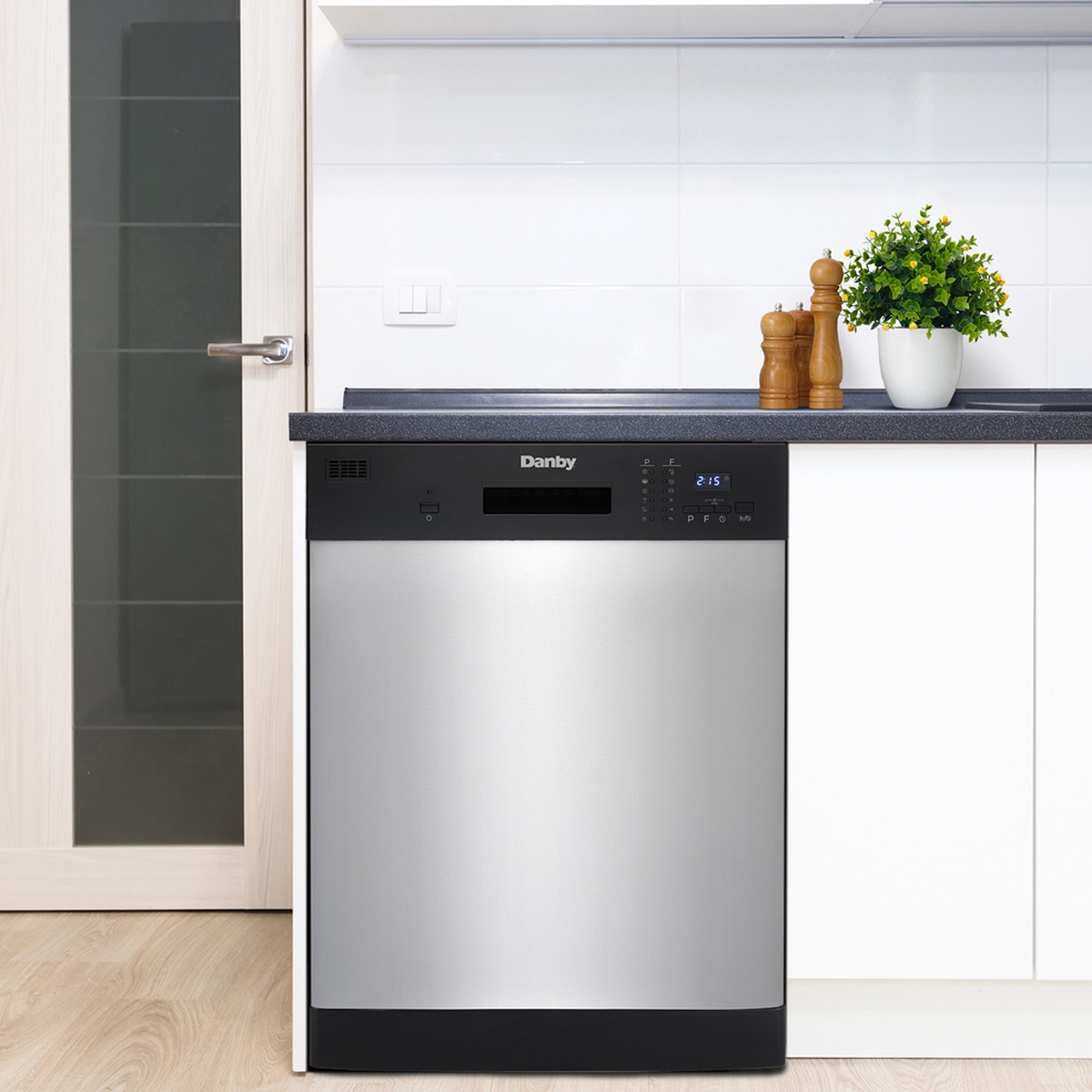 Danby DDW2404EBSS dishwasher installed flush under a dark countertop in a modern white kitchen with wood floors