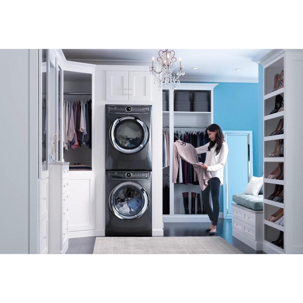 Electrolux titanium front-load washer and dryer stacked in a bright walk-in closet laundry setup while a woman sorts freshly washed clothes