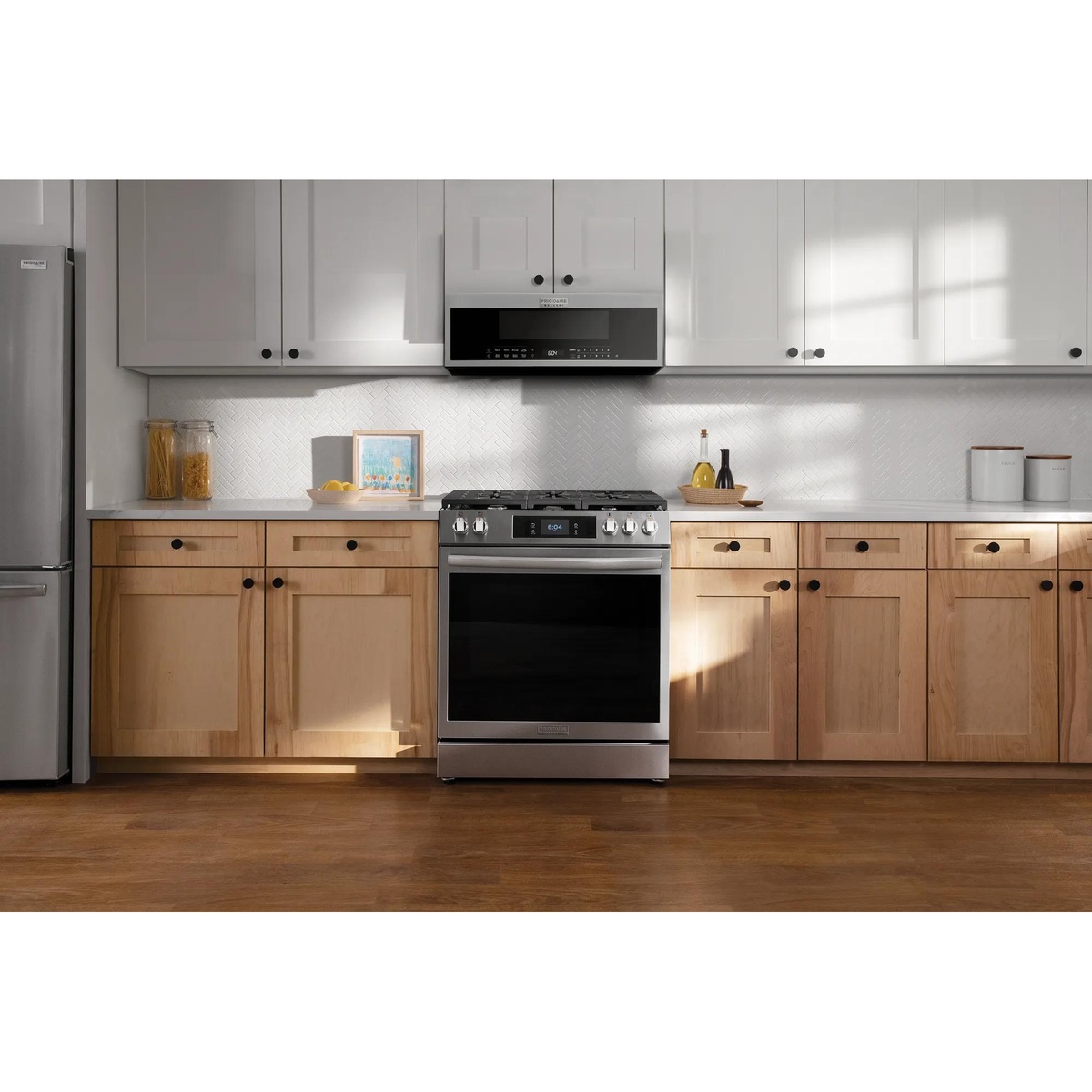 Frigidaire Gallery GMOS1266AF low-profile over-the-range microwave installed above a gas range in a bright modern kitchen with white upper cabinets and natural wood lower cabinets