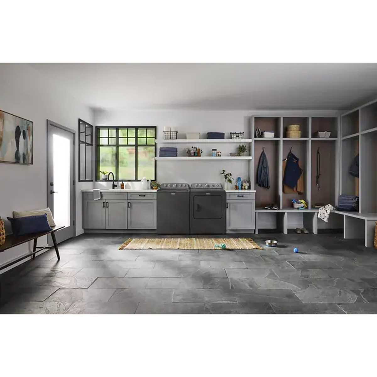 A Maytag washer and dryer set installed side by side in a bright laundry room with cabinets, shelves, and hanging storage